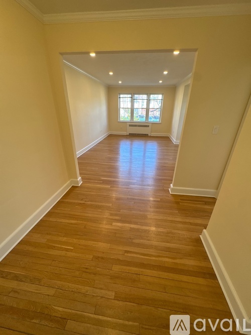 A long hallway with wooden floors and a window at the end.
