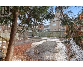 A backyard with a fence, trees, and a building in the background.
