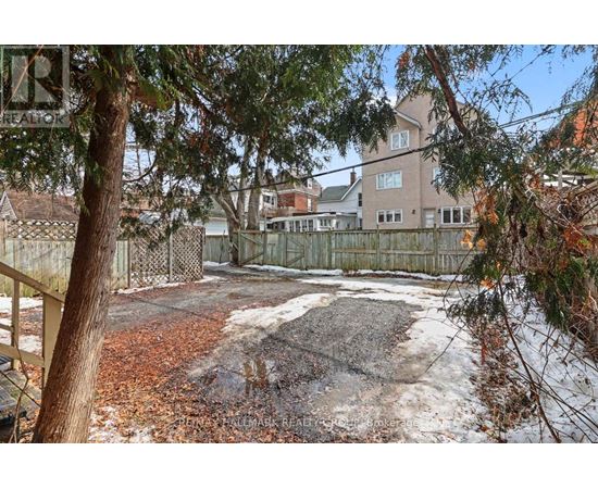 A backyard with a fence, trees, and a building in the background.