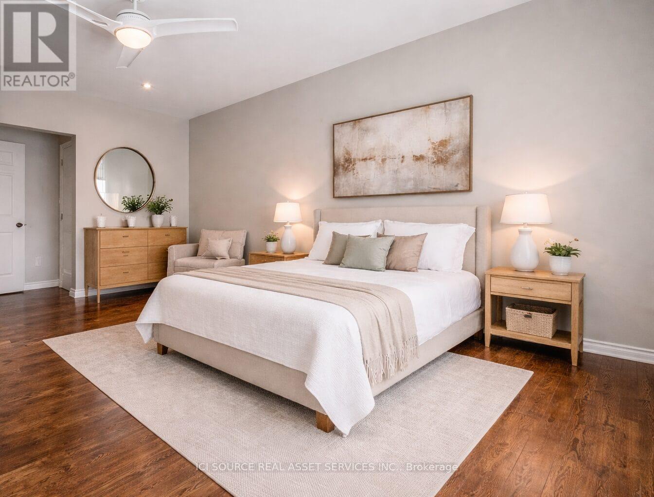 A bedroom with a large bed, a side table with a plant, and a painting on the wall.