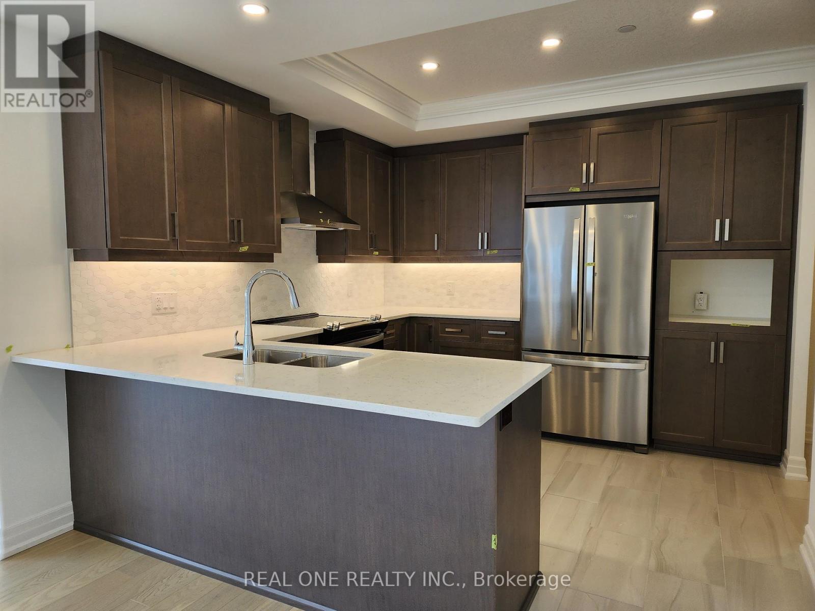 A modern kitchen with dark brown cabinets and a stainless steel refrigerator.
