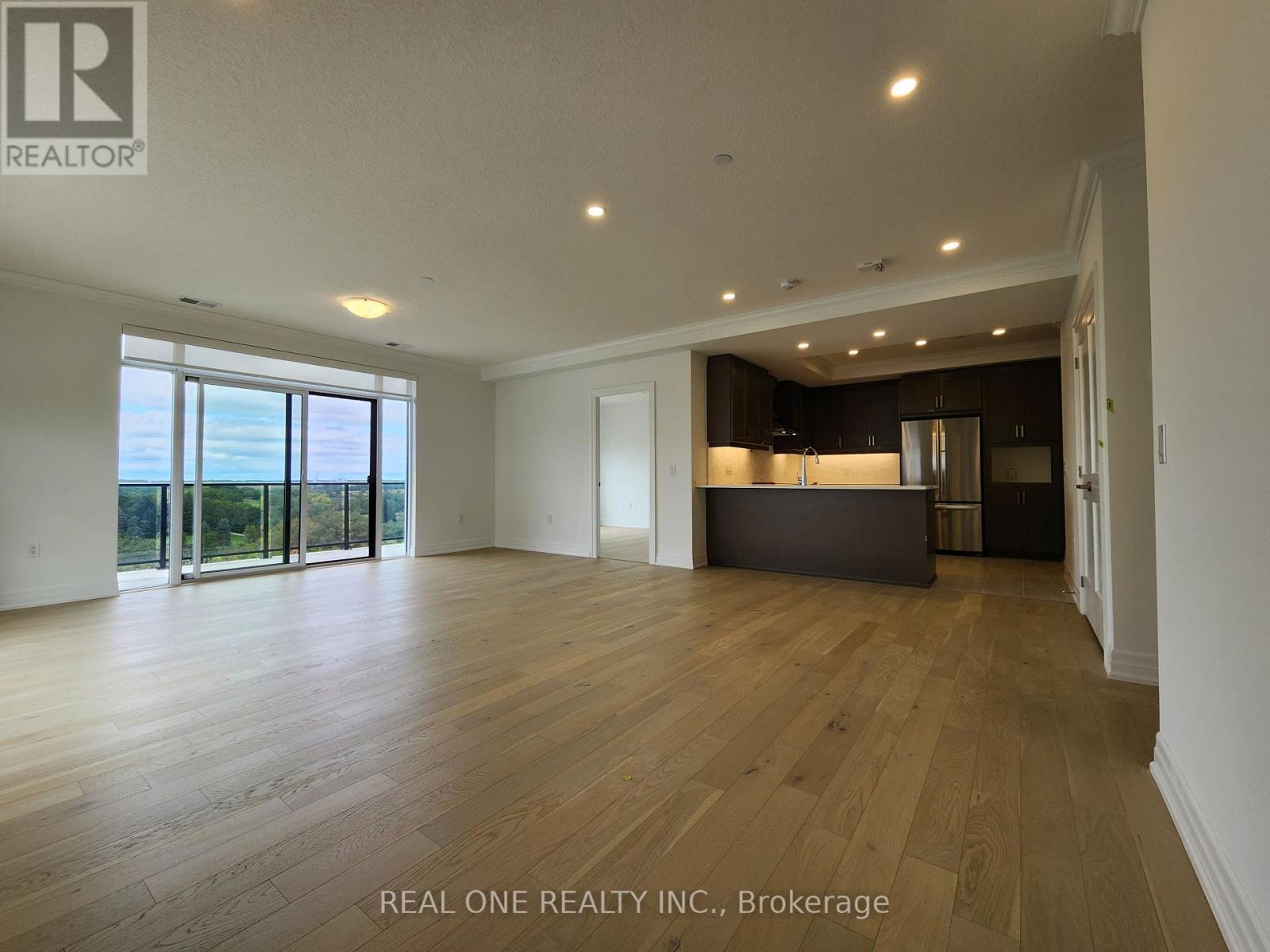 A spacious room with wooden flooring and a large window overlooking a landscape.