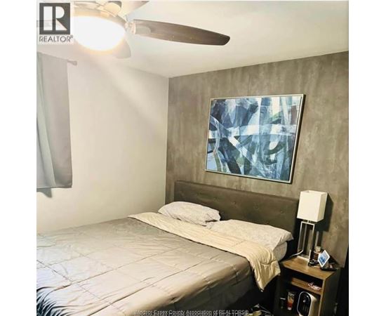 A bedroom with a bed, nightstand, and a painting on the wall.