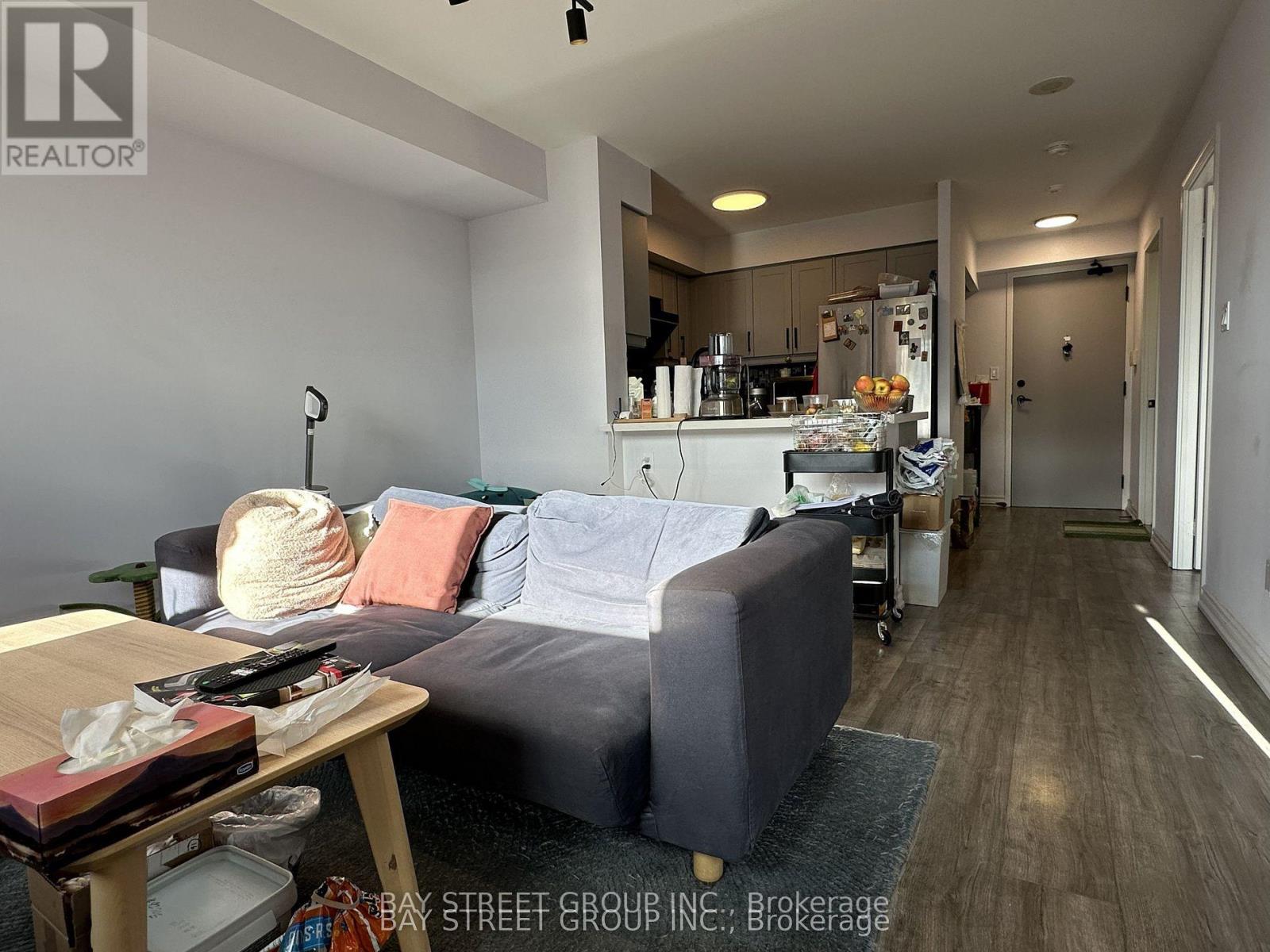 A living room with a grey couch and a kitchen area in the background.