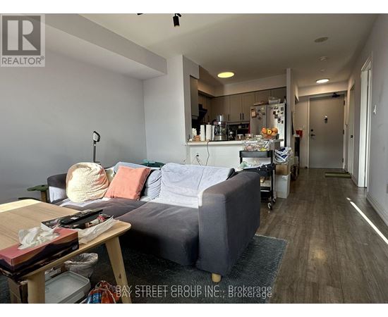 A living room with a grey couch and a kitchen area in the background.