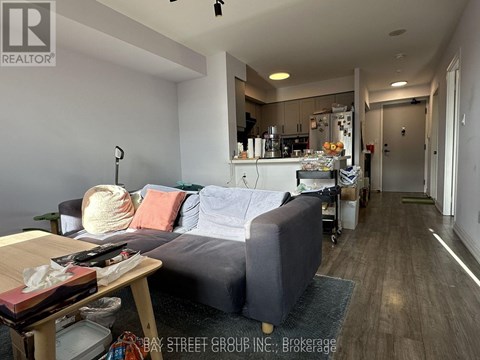 A living room with a grey couch and a kitchen area in the background.