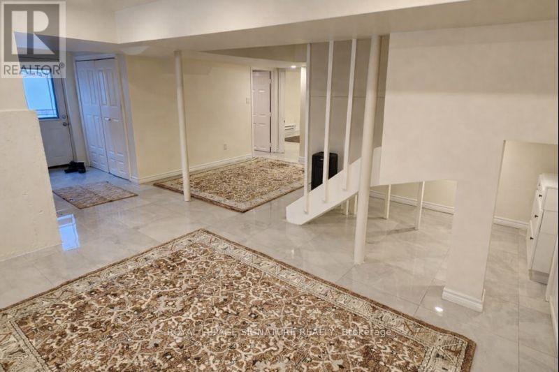 A large, empty room with a rug on the floor and a staircase on the right side.