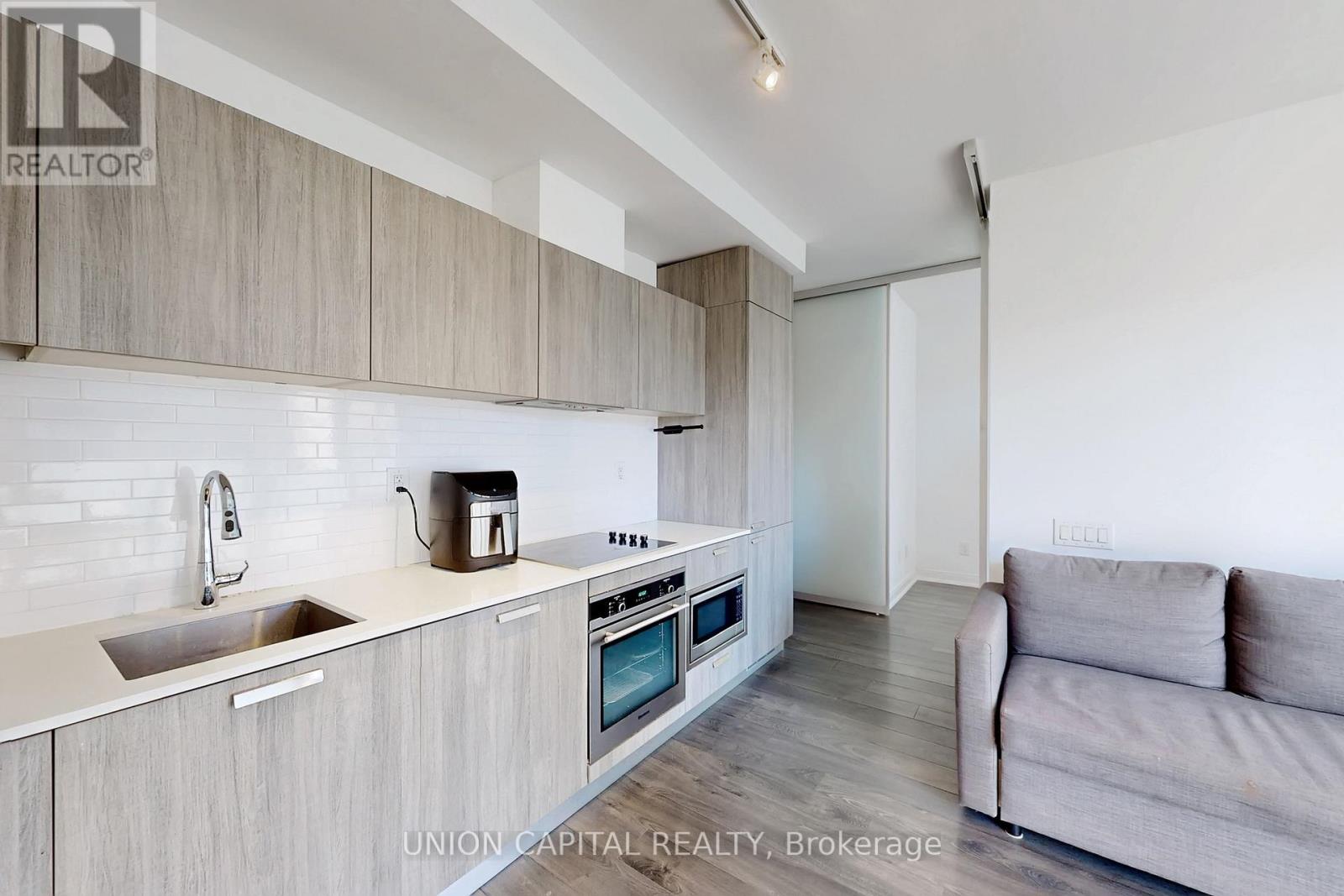 A modern kitchen with wooden cabinets and a grey couch.