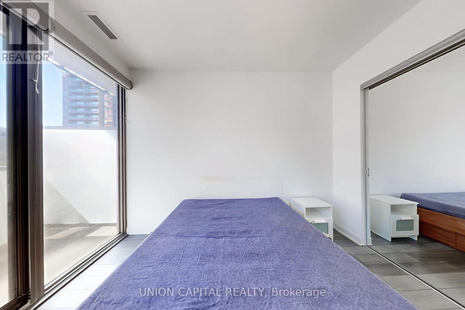 A bedroom with a long bed and a window with a view of the city.