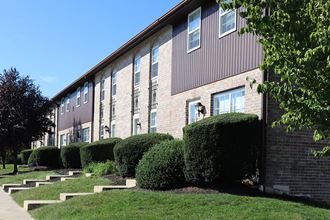 the side of a brick apartment building with stairs and hedges