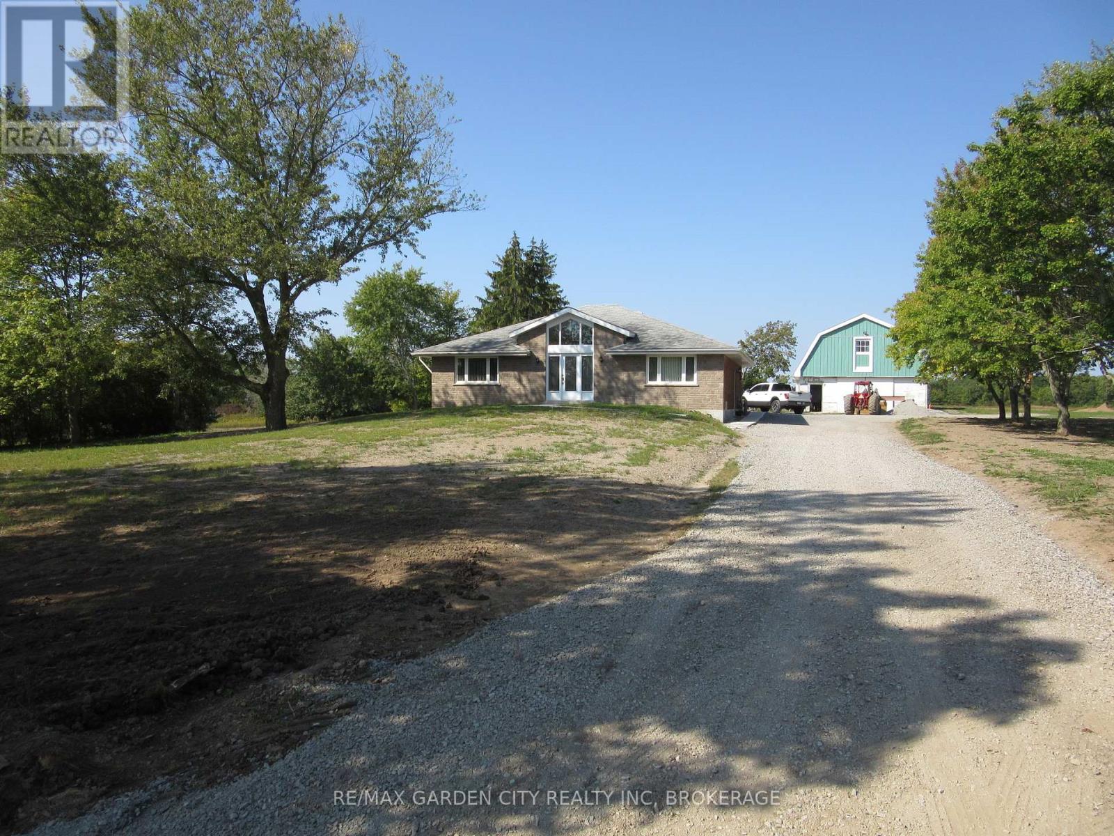 A gravel driveway leads to a house with a green lawn and trees.
