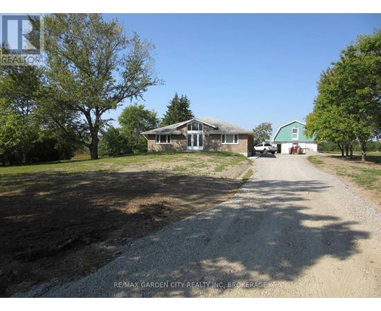 A gravel driveway leads to a house with a green lawn and trees.