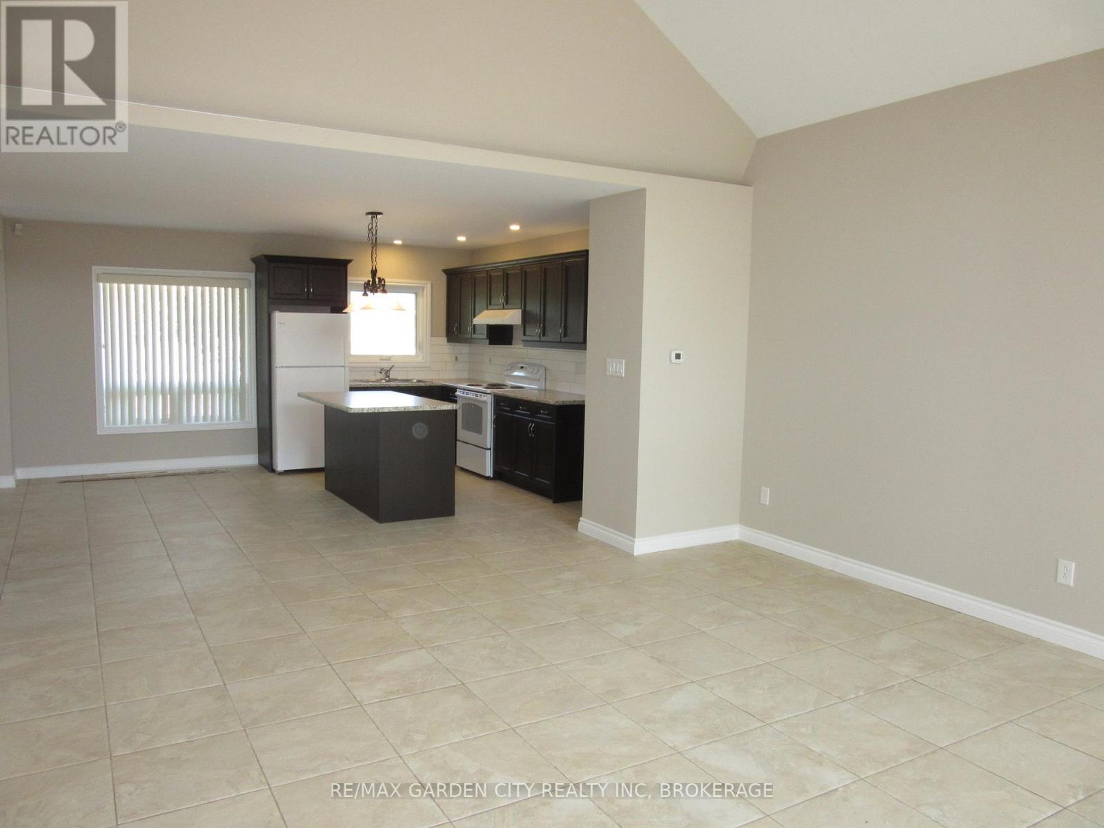 A kitchen area with a sink, stove, and refrigerator in a room with tiled flooring.