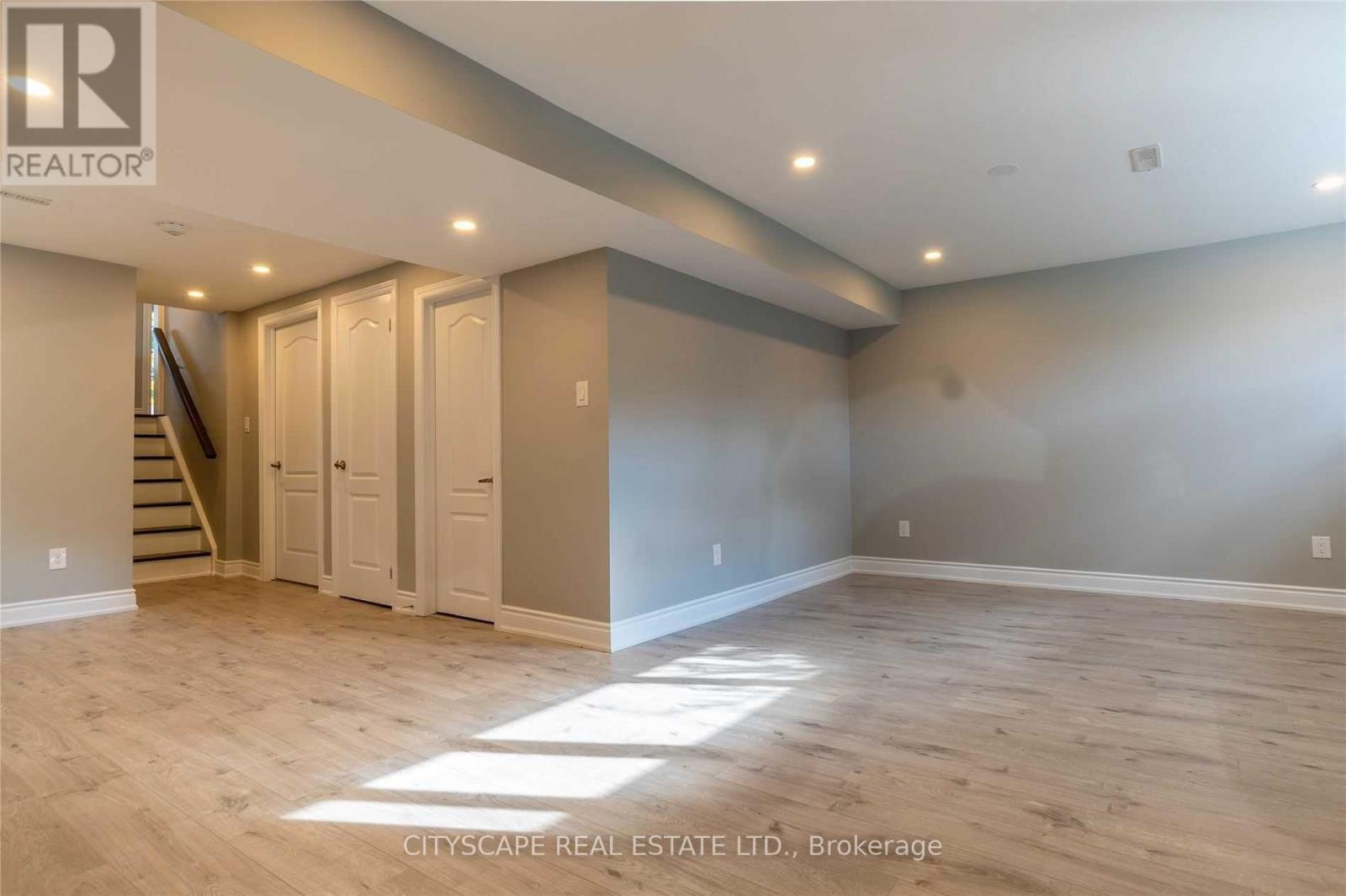 A spacious room with wooden flooring and a staircase leading to another level.