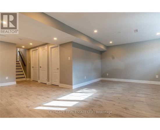 A spacious room with wooden flooring and a staircase leading to another level.