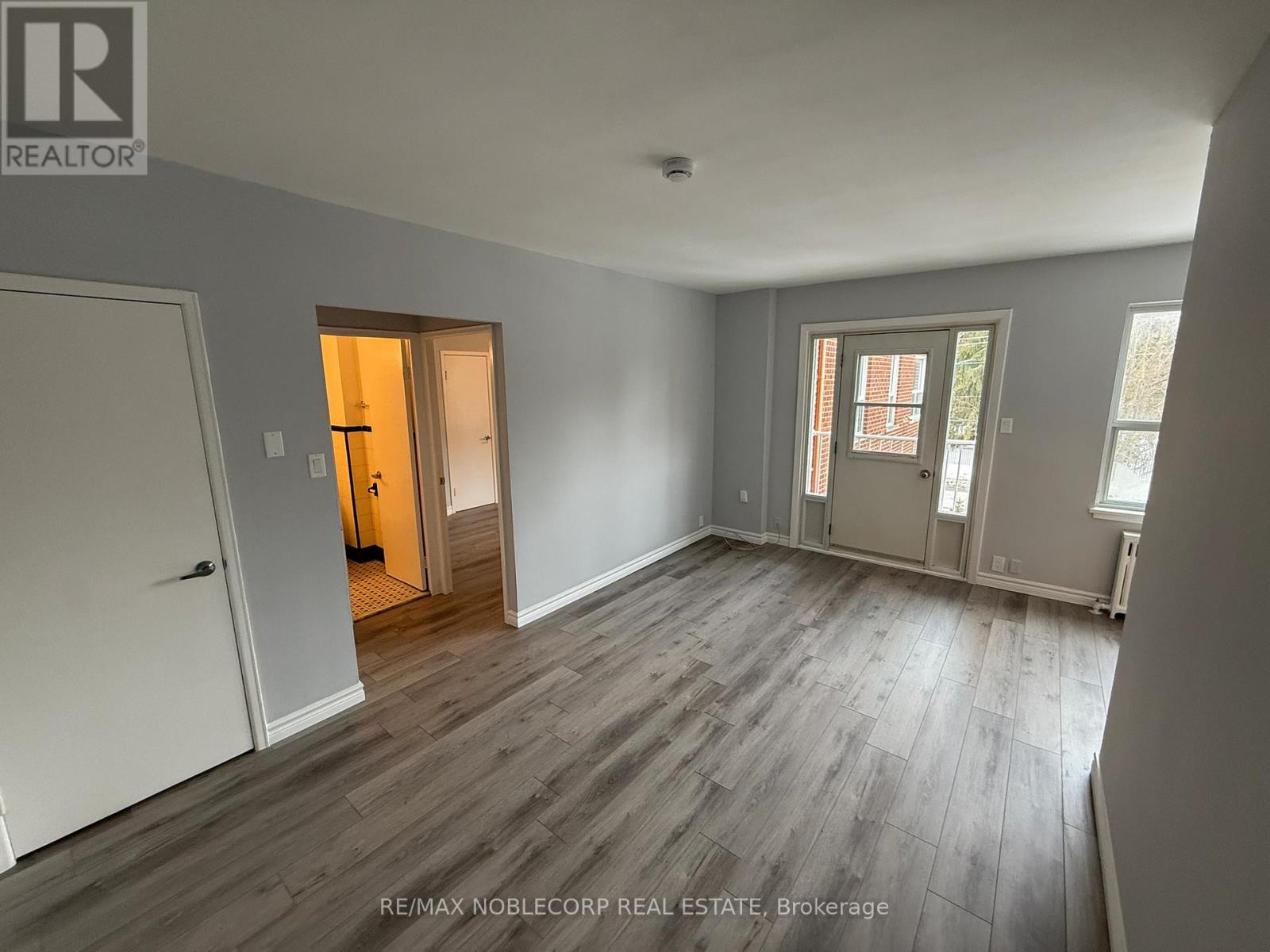 A room with grey walls and wooden flooring with a white door on the left and a window on the right.