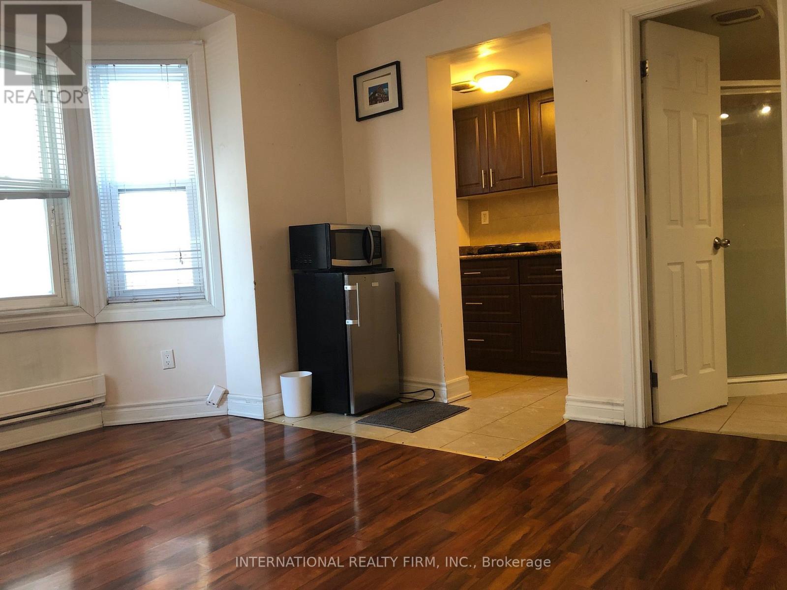 A room with a black refrigerator and wooden floors.