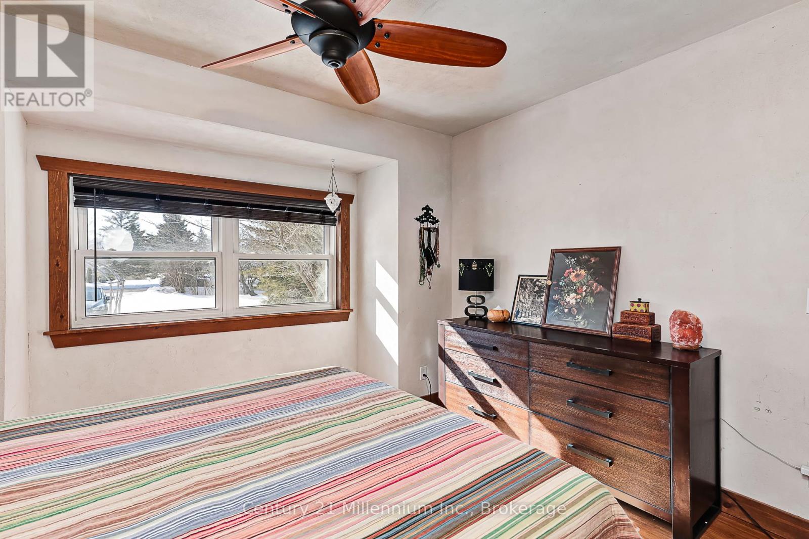 A bedroom with a striped bedspread, a ceiling fan, and a dresser with a mirror.