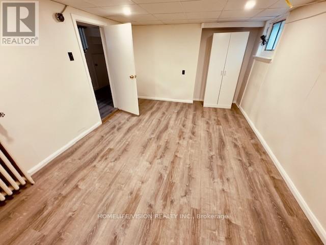 A room with wooden flooring and white walls, with a door open to another room.