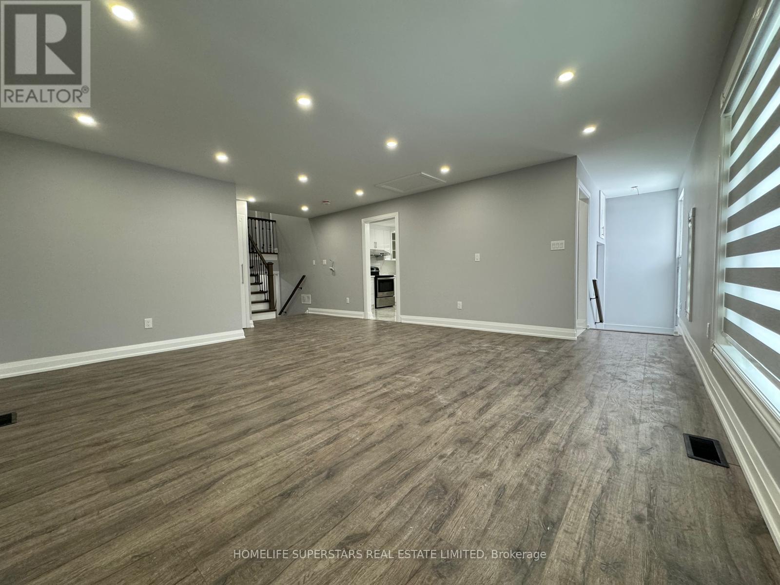 A spacious room with wooden flooring and a staircase in the background.