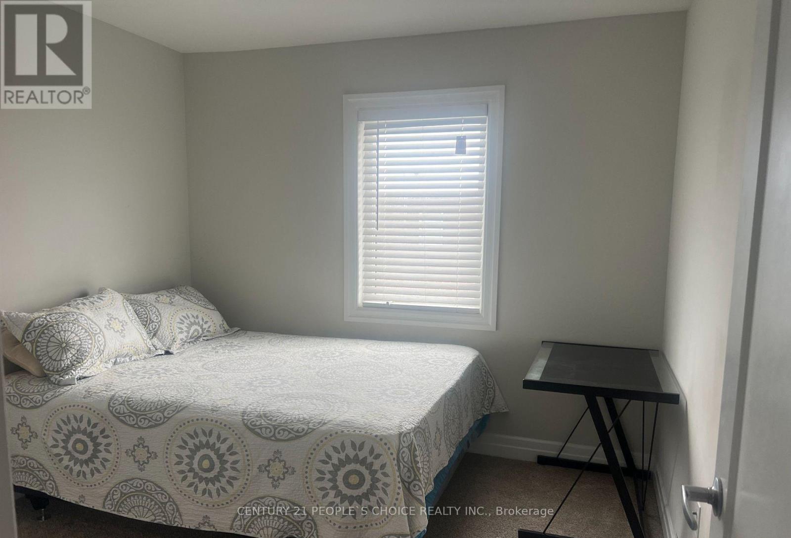 A bedroom with a bed, a small table, and a window with blinds.