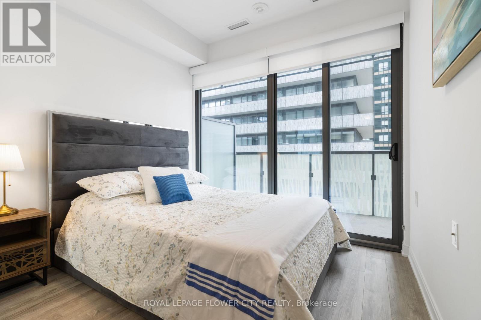 A bedroom with a large bed and a view of a building outside the window.
