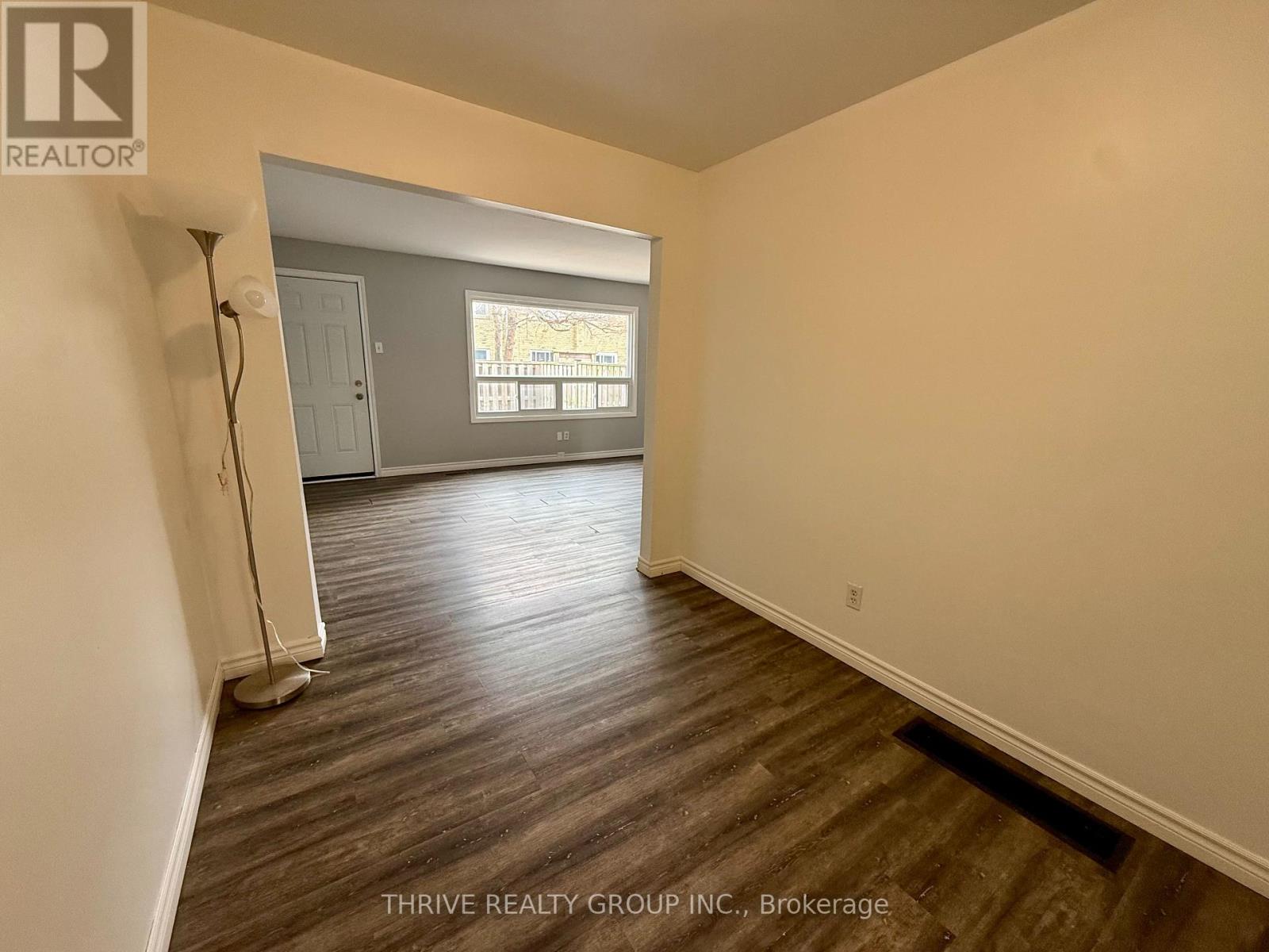 A room with wood flooring and a window overlooking a tree-filled street.
