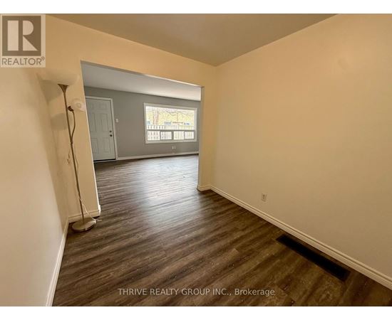 A room with wood flooring and a window overlooking a tree-filled street.