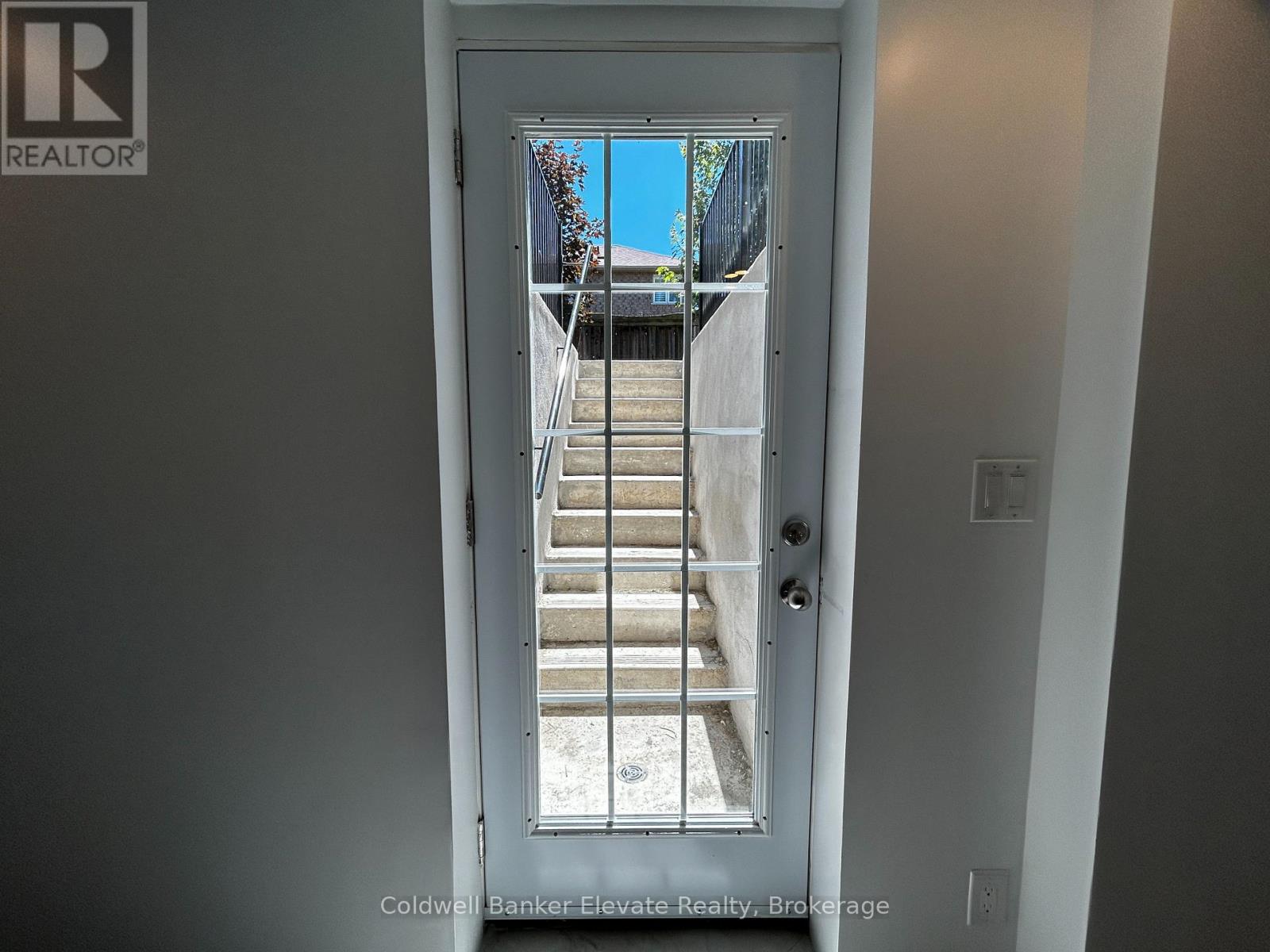 A door with a glass window showing a staircase and a blue sky.
