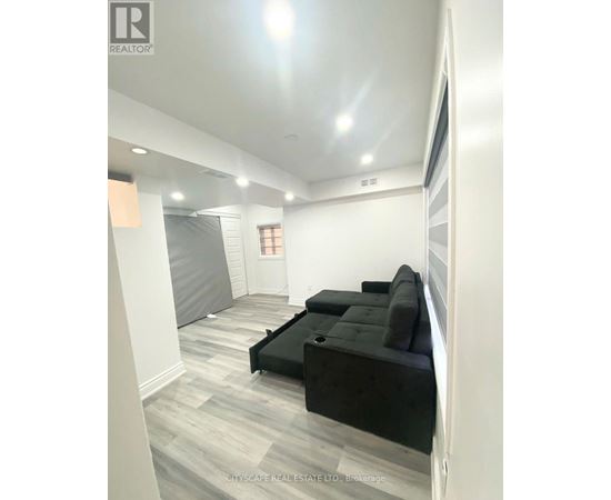 A living room with a black couch and grey carpet.