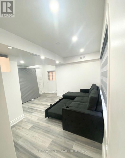 A living room with a black couch and grey carpet.