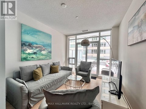 A living room with a grey couch and a painting on the wall.