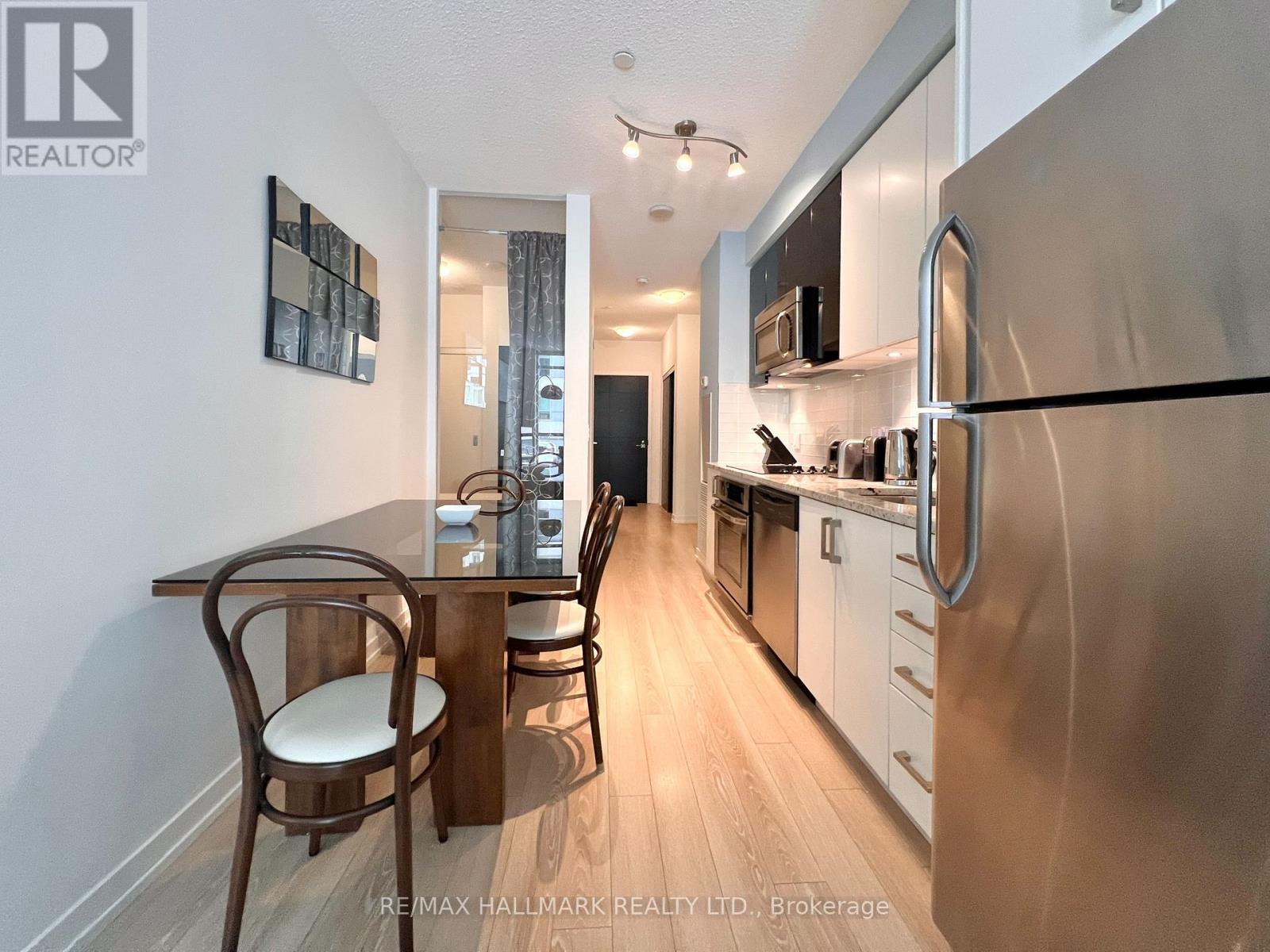 A kitchen with a dining table and chairs in the foreground and a refrigerator in the background.