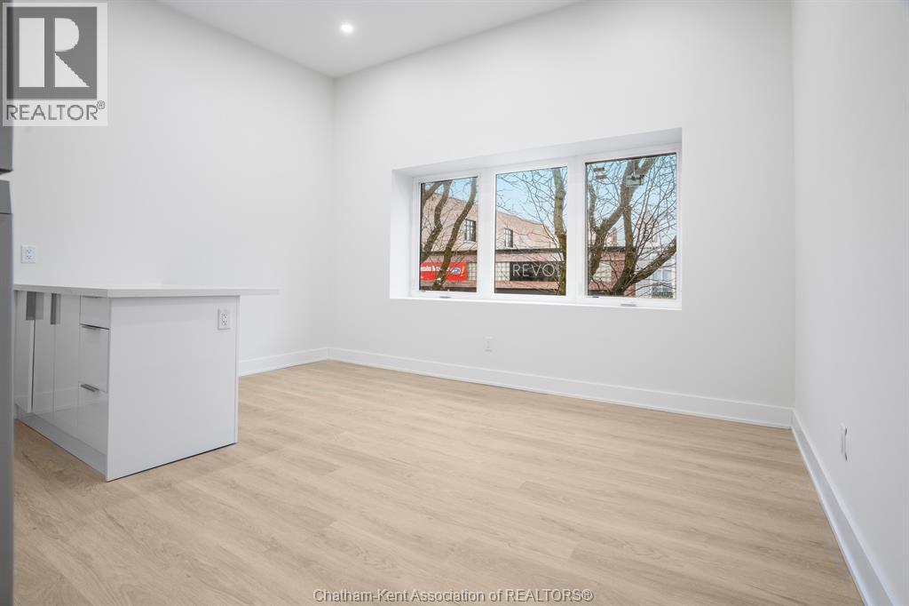 A white room with a wooden floor and a window showing a view of a tree and a building.
