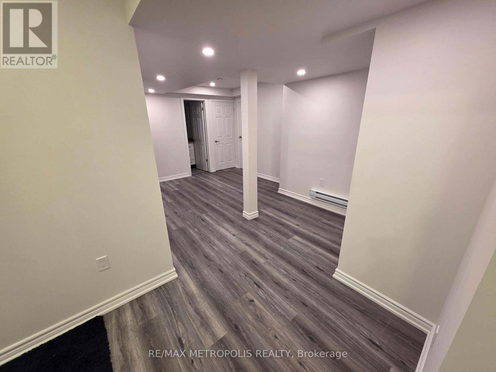 A room with wooden flooring and white walls, with a door at the end of the hallway.