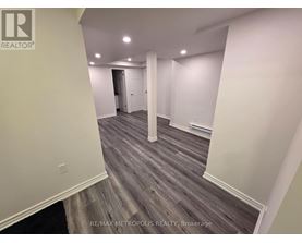 A room with wooden flooring and white walls, with a door at the end of the hallway.