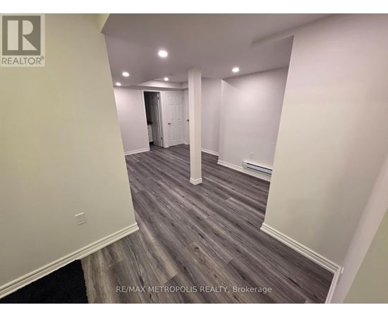 A room with wooden flooring and white walls, with a door at the end of the hallway.