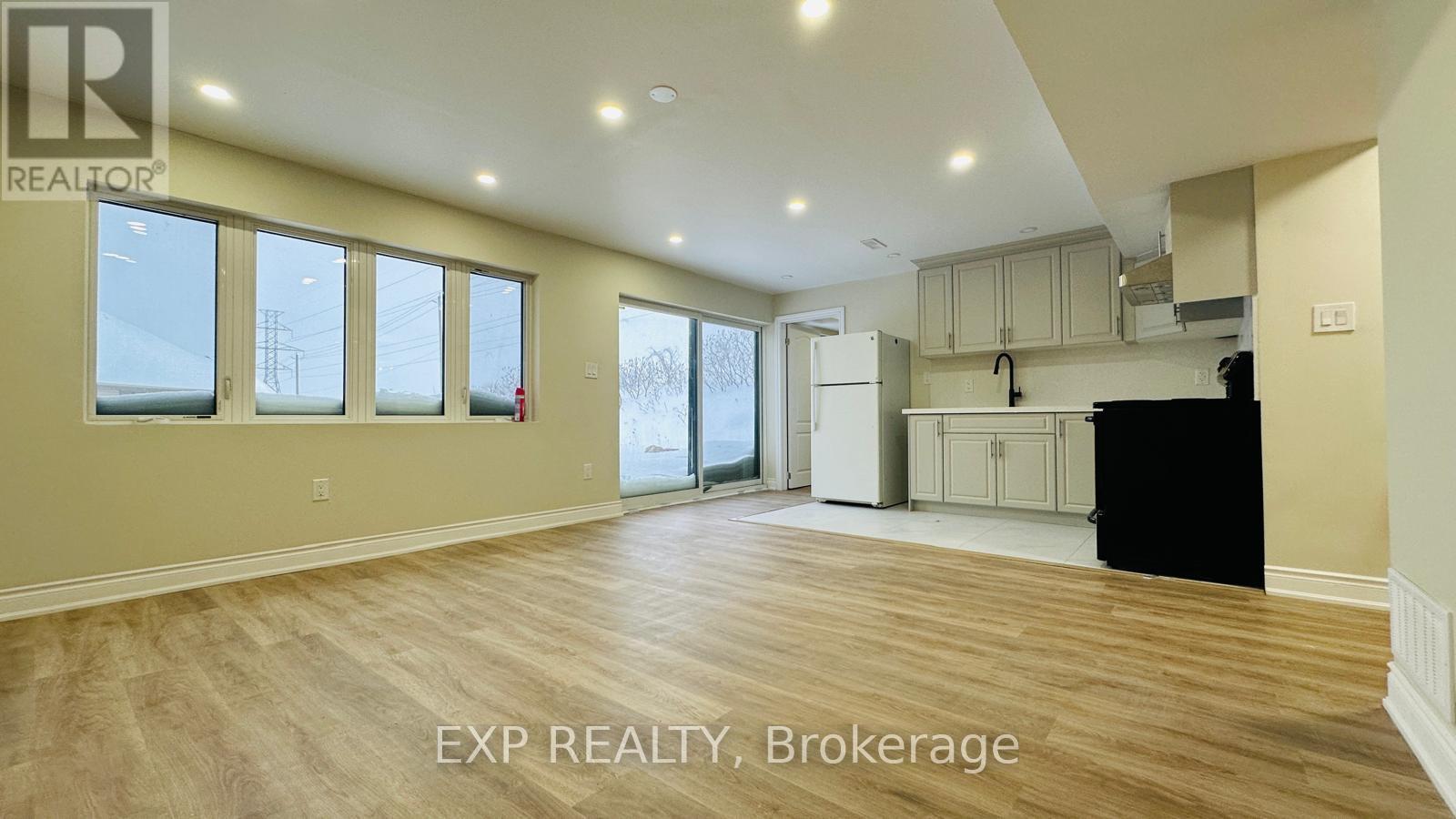 A spacious room with wooden flooring and large windows.