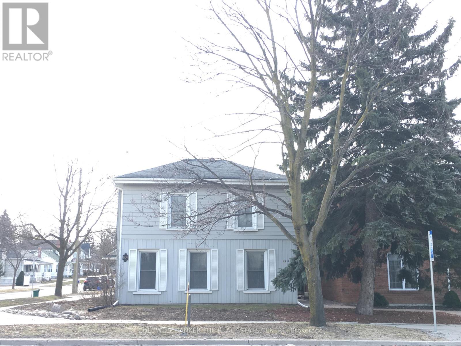 A grey house with a tree in front of it.