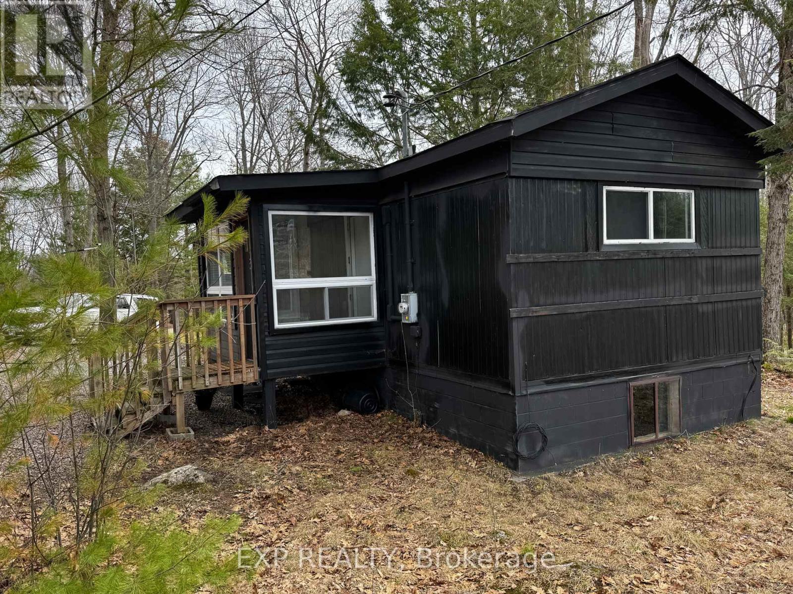A black cabin with a porch is surrounded by trees.
