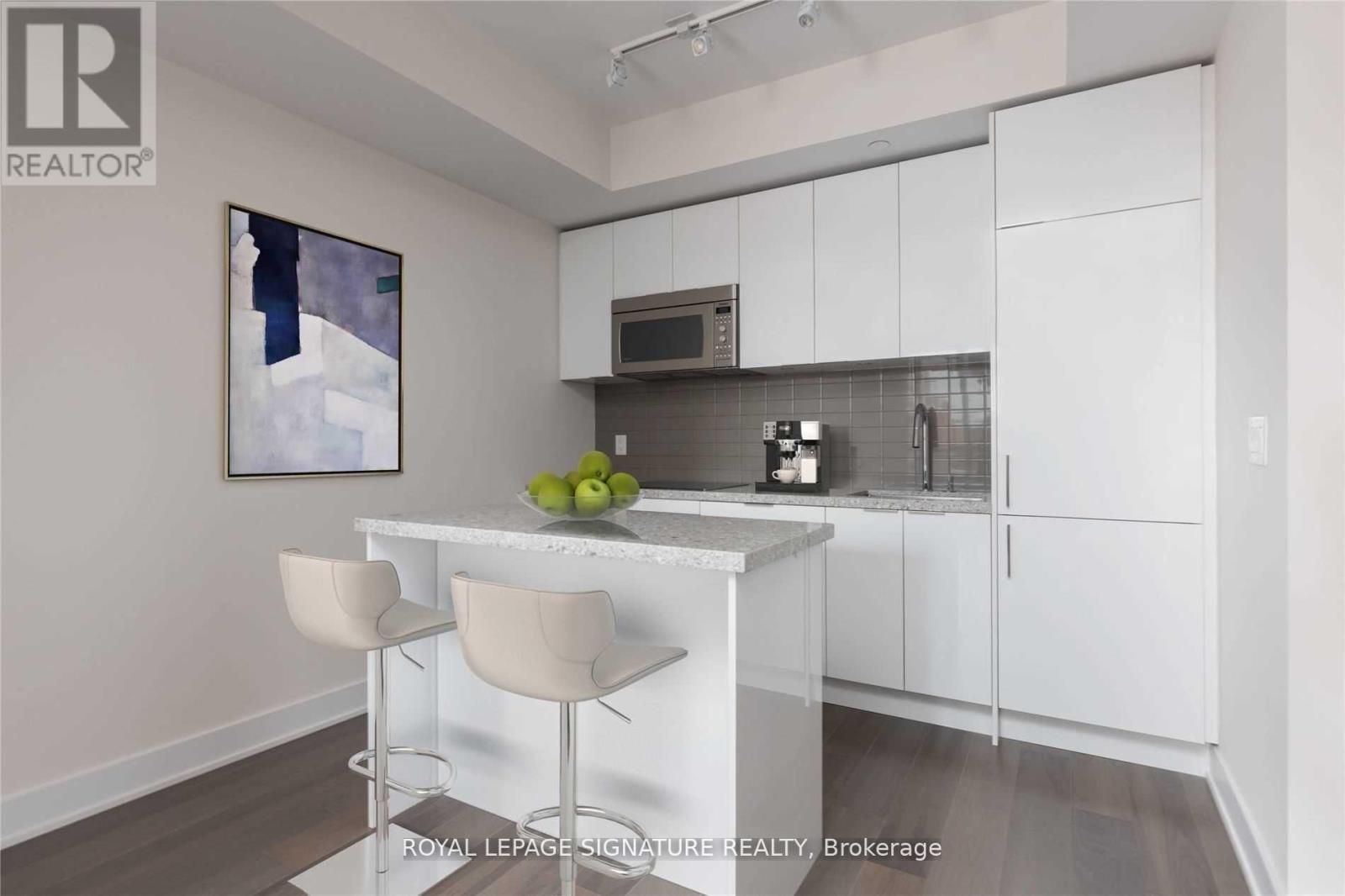 A white kitchen with a fridge, microwave, and a counter with two chairs.