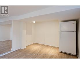 A white refrigerator is in a room with wood flooring and white walls.