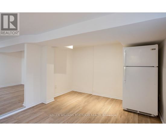 A white refrigerator is in a room with wood flooring and white walls.