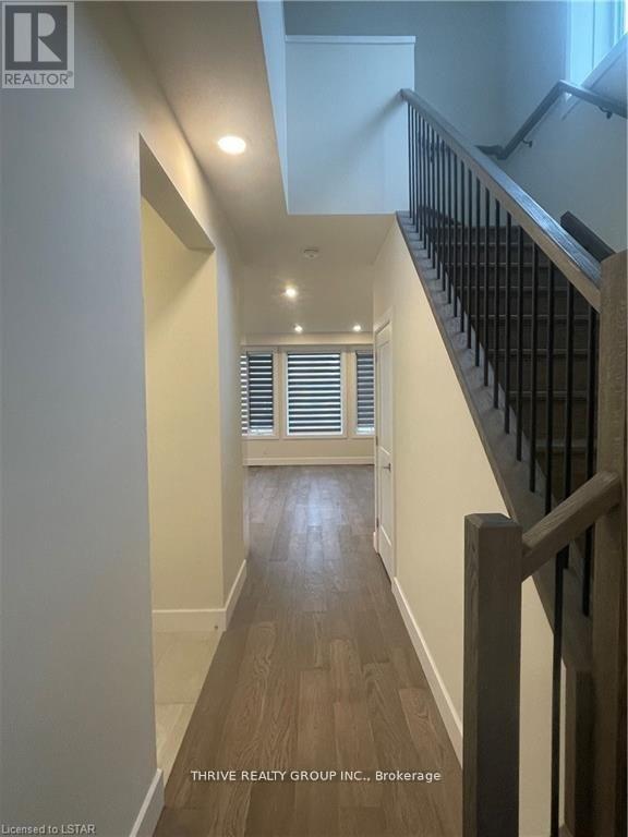 A hallway with a staircase on the right and a window with blinds on the left.