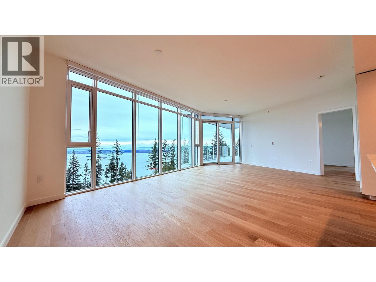 A spacious room with wooden floors and large windows overlooking the ocean.