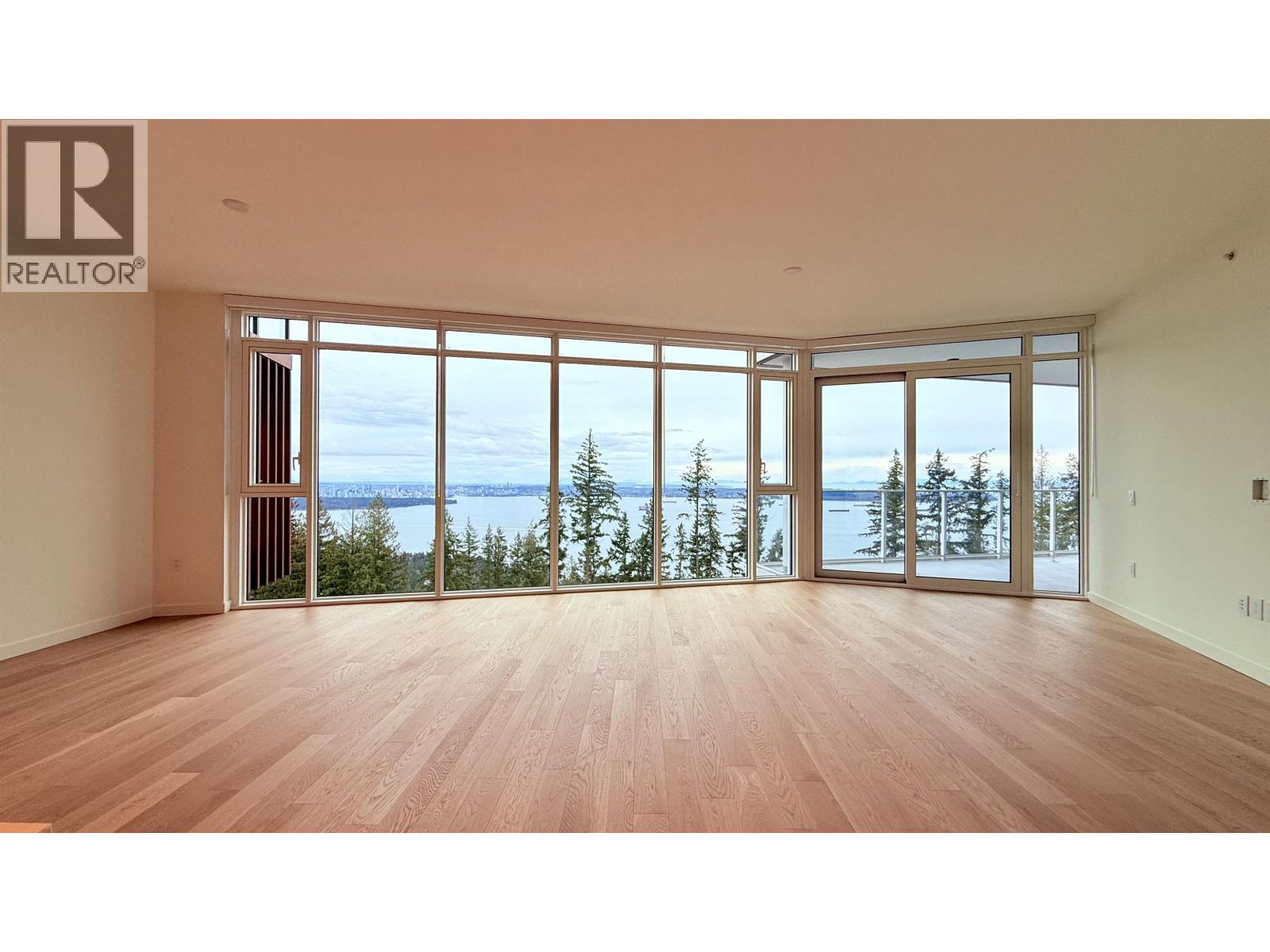 A large empty room with a view of the lake and trees outside the windows.