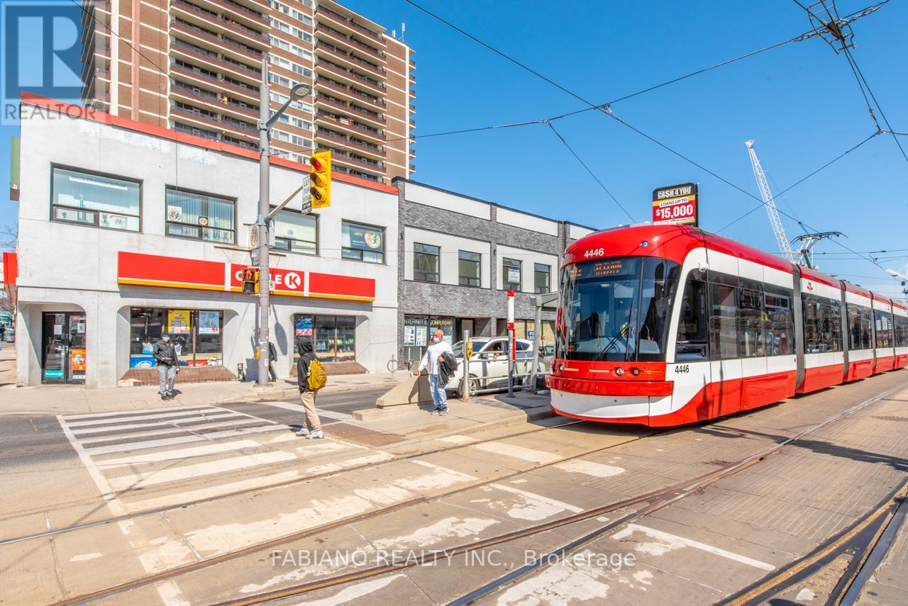 A red and white streetcar is on the tracks in front of a building with a sign that says "Shoppers Drug Mart".