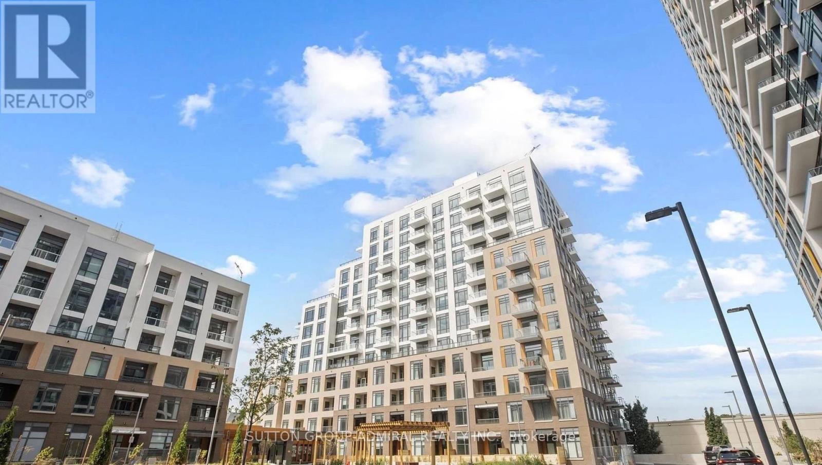 A modern multi-story building with a glass facade stands in the foreground of a sunny day.