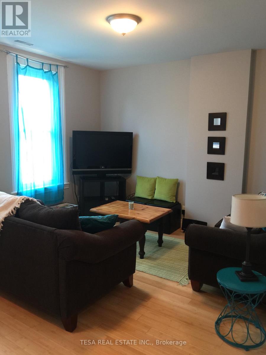 A living room with a black couch, a green cushion, a television, and a lamp.