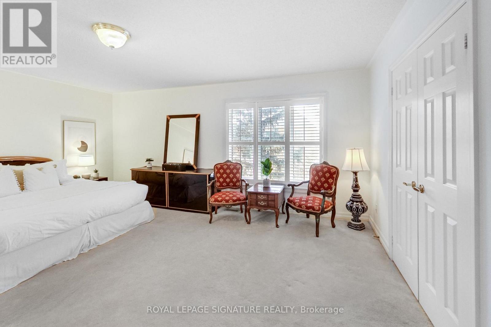 A white bedroom with a bed, dresser, chair, and mirror.
